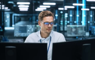 Ein Systemadministrator sitz fokussiert vor seinen Bildschirmen und hat dank Monitoring und Netzwerktransparenz alles im Griff